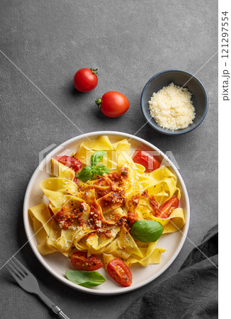 Tagliatelle pasta with tomato sauce, basil and parmesan cheese in a plate on a dark background. 121297554