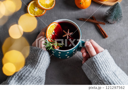 Hands in a sweater holding a cup of mulled wine with orange, cinnamon and rosemary  121297562