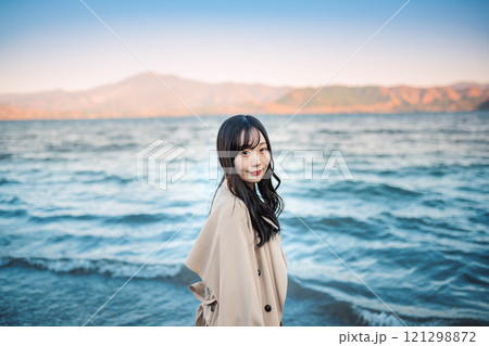 青空と湖とトレンチコートの若い女性 121298872
