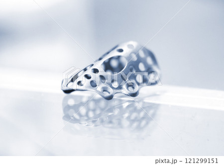 Titanium dental membranes for directed bone regeneration printed on 3D printer on white background. Membrane for lower jaw printed from biocompatible titanium powder. Implants and prostheses 121299151
