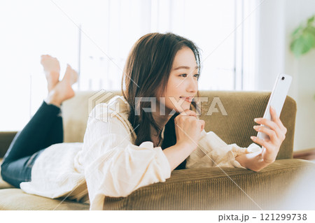ソファに寝転がってスマホを見る女性 121299738