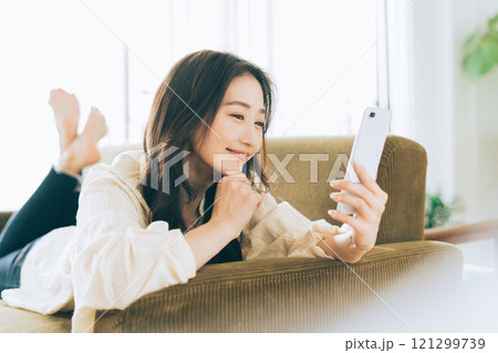 ソファに寝転がってスマホを見る女性 121299739