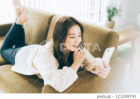 ソファに寝転がってスマホを見る女性 121299741