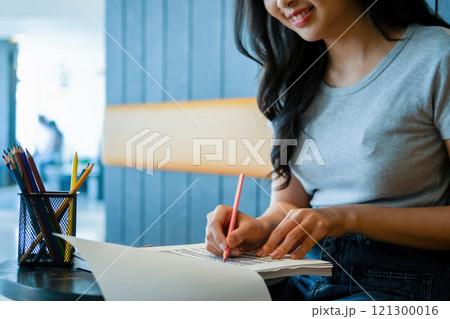 Young woman engages in note-taking at workspace. Young woman engages in note-taking at workspace. 121300016