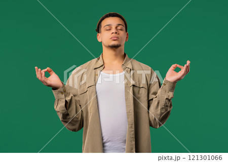 Calm teen guy relaxing, meditating, refuses stress. Breathes deeply on green Calm teen guy relaxing, meditating, refuses stress. Breathes deeply on green 121301066