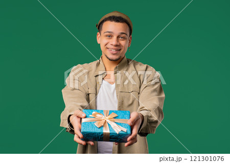 Stylish Excited Man Holding Gift Box And Gives It By Hands To Camera on green. 121301076