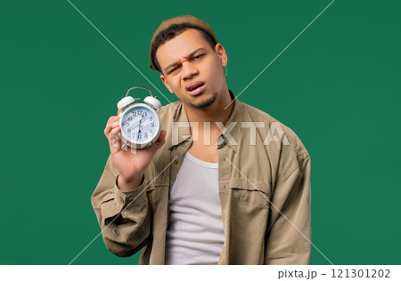 Woken up by alarm clock sleepy young man holding it in hand. green background 121301202