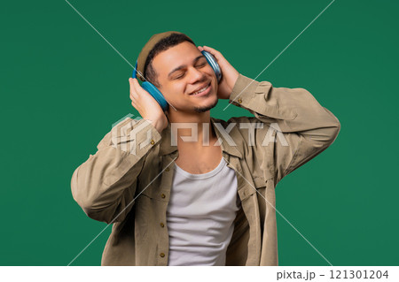 Hipster positive man listening music, enjoying with headphones, green studio 121301204