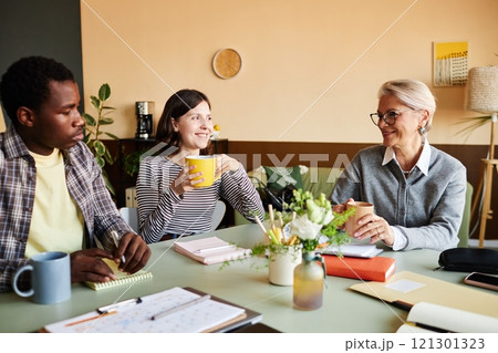 Medium shot of multigenerational team of positive employees and mature female boss networking over cup of coffee during break in office, copy space 121301323