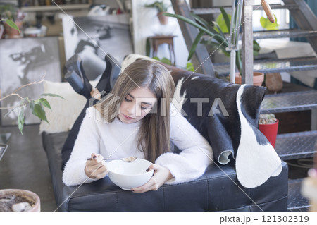 Young woman enjoying cereal while relaxing on a modern sofa. 121302319