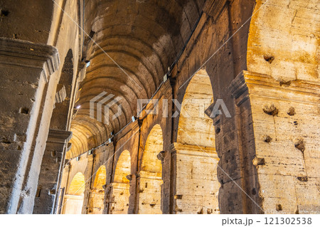 Visitors explore the interior of the Colosseum, admiring its impressive arches and stonework, while the sunlight highlights the ancient structure's history in Rome, Italy. 121302538