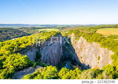 Velka Amerika Quarry showcases its breathtaking cliffs and lush greenery on a sunny morning in Czechia. The tranquil water at the bottom reflects the beauty of surrounding this stunning landscape. Velka Amerika Quarry showcases its breathtaking cliffs and lush greenery on a sunny morning in Czechia. The tranquil water at the bottom reflects the beauty of surrounding this stunning landscape. 121302540