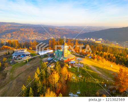 The Tanvaldsky Spicak Lookout Tower stands amidst vibrant autumn foliage in the Jizera Mountains, offering stunning views of the surrounding landscape in the evening light. 121302569