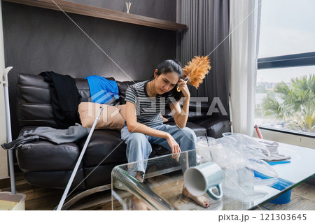 Shocked woman with messing home while cleaning house. Young girl surrounded by many of clothes and trash 121303645