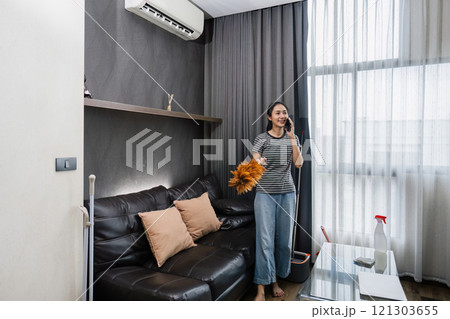 Young woman chit chat with friend on mobile while cleaning house on weekend Young woman chit chat with friend on mobile while cleaning house on weekend 121303655