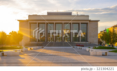 The sun rises, casting golden light on the Janacek Theatre in Brno, highlighting its architectural features and the tranquil atmosphere of the surrounding plaza. 121304221