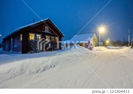 Electric light in windows of rural house in snowy evening village on Christmas Eve in northern Europe. Electric light in windows of rural house in snowy evening village on Christmas Eve in northern Europe. 121304411