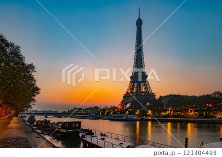 The Eiffel Tower rises majestically over the Seine River at dawn in Paris, casting reflections on the water as the sky lightens, creating a serene and enchanting atmosphere. 121304493