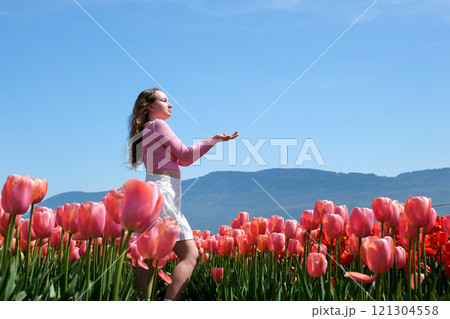 Young woman tourist in pink dress and straw hat standing in blooming tulip field. Spring time 121304558