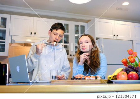 Young pretty woman sitting at her kitchen eat sushi at table home working with a laptop Young pretty woman sitting at her kitchen eat sushi at table home working with a laptop 121304571