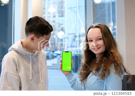 boy girl green screen advertising Happy girl showing a blank phone screen to a friend on a couch at home 121304583