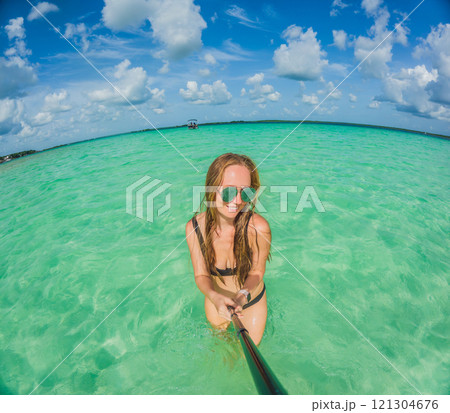 Woman standing in the crystal-clear waters of Lake Bacalar, Mexico, enjoying the serene beauty of the landscape. Tranquil moment in nature, outdoor escape, and relaxation concept 121304676