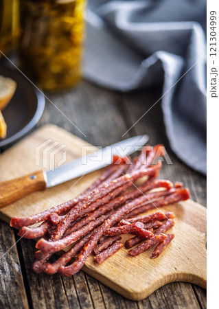 Smoked kabanos. Mini dried thin sausages on cutting board on wooden table. 121304999