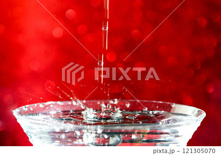 Close-up of water drop falling into a glass on red background	 121305070