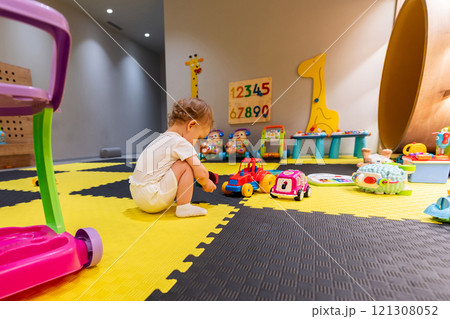 oddler sitting on a playmat surrounded by toys in a vibrant playroom. Concept of early childhood development and fun activities oddler sitting on a playmat surrounded by toys in a vibrant playroom. Concept of early childhood development and fun activities 121308052
