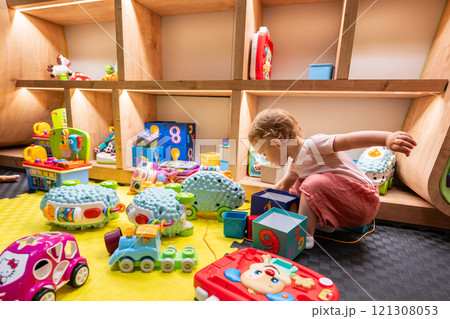 Little girl playing with toys in a cozy playroom. Concept of childhood learning and fun activities Little girl playing with toys in a cozy playroom. Concept of childhood learning and fun activities 121308053