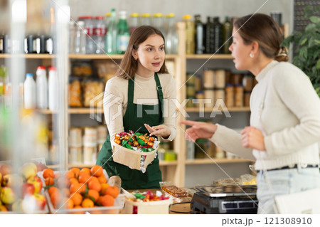 Female seller offers to buy candies to woman in interior of grocery supermarket Female seller offers to buy candies to woman in interior of grocery supermarket 121308910