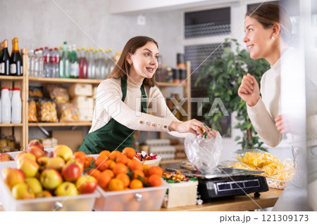 Female vendor weighs candies on scales and sells candies to customer Female vendor weighs candies on scales and sells candies to customer 121309173
