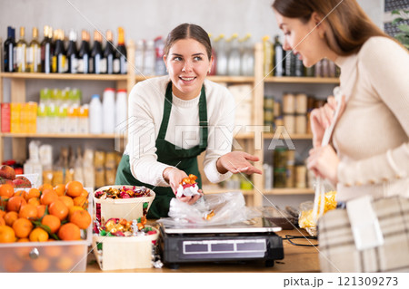 Female vendor weighs candies on scales and sells candies to customer Female vendor weighs candies on scales and sells candies to customer 121309273