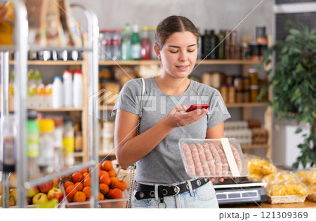 Girl shopper scanning QR code on raw sausages label in grocery department of supermarket Girl shopper scanning QR code on raw sausages label in grocery department of supermarket 121309369
