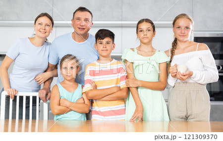 Happy dad and mum with three daughters and son is standing near kitchen table. 121309370