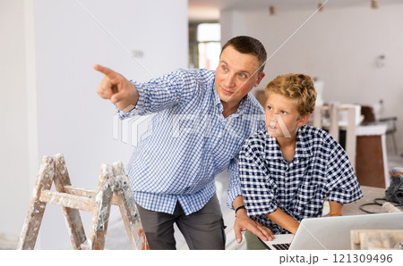 Man architect and boy using laptop while discussing working process in house being renovated 121309496