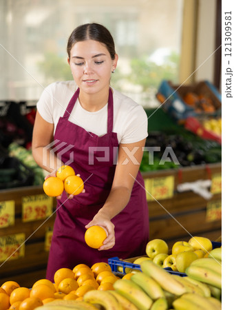 Girl seller was distracted for minute and stands smiling with ripe oranges in hands Girl seller was distracted for minute and stands smiling with ripe oranges in hands 121309581