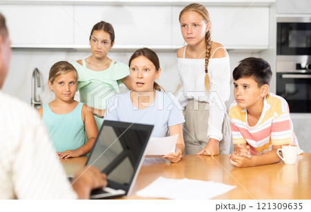Man with laptop does remote work, frustrated wife reads letter, and alarmed children stand nearby 121309635
