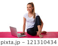Sporty young smiling woman sitting in pink yoga mat and using laptop, isolated on white background 121310434