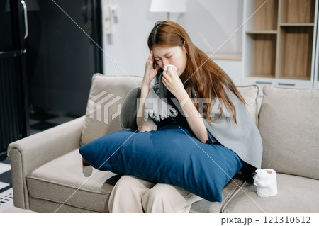 Young Asian woman suffering from flu symptoms, covered with a blanket on a sofa. Concept of illness, healthcare Young Asian woman suffering from flu symptoms, covered with a blanket on a sofa. Concept of illness, healthcare 121310612