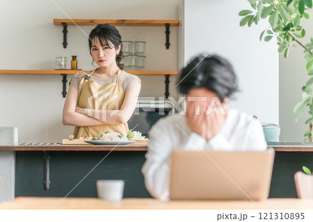 テレワークする夫をキッチンで不機嫌そうに睨む主婦・妻(夫婦喧嘩・イライラ・離婚) テレワークする夫をキッチンで不機嫌そうに睨む主婦・妻(夫婦喧嘩・イライラ・離婚) 121310895