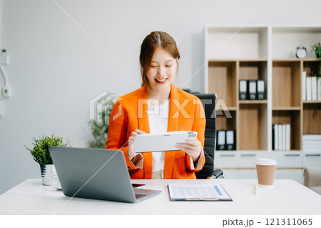 Asian Businesswoman Analyzing Finance on Tablet and Laptop at modern Office Desk tax 121311065