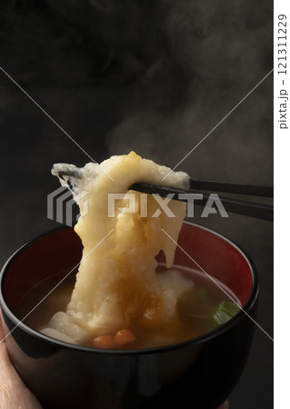 お雑煮のお椀を手で持ち餅を箸で持ち上げる 121311229