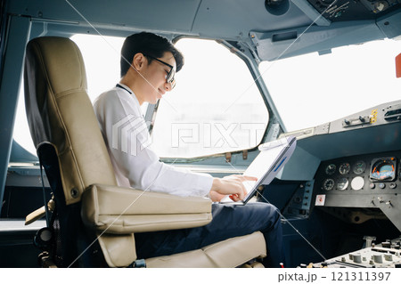 Asian Confident male pilot in uniform leaning at the passenger seat while standing inside of the airplane flight 121311397