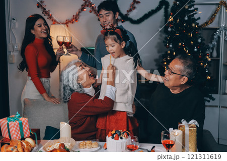 Multi-Generation Family Celebrate Christmas At Home Wearing Santa Hats And Antlers Opening Presents 121311619
