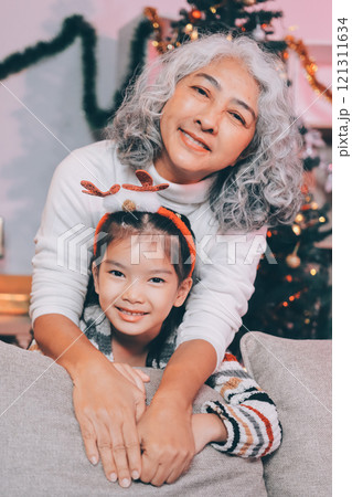 Happy family on Christmas morning. Affectionate grandmother and cheerful granddaughter open a holiday gift together at home 121311634
