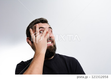 Man peeking through fingers with surprised expression. 121312058