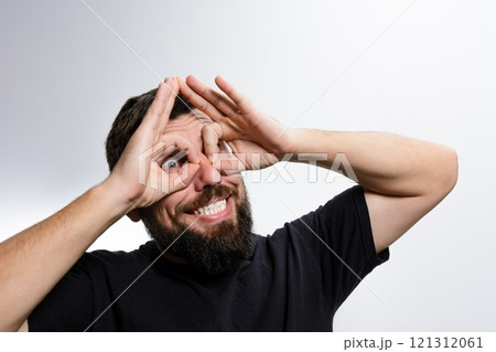 Playful man makes binoculars with hands, looking through with wide smile. 121312061