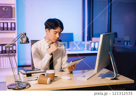 Businessman drinking coffee to get some energy for working overtime sitting at desk using computer and doing overtime 121312535