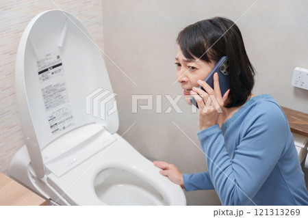 トイレのトラブルで水道業者に電話する女性 トイレのトラブルで水道業者に電話する女性 121313269